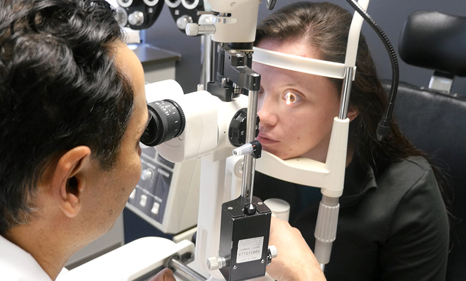 Closeup of a Dr Shah looking through examination equipment into a female patient’s eyes