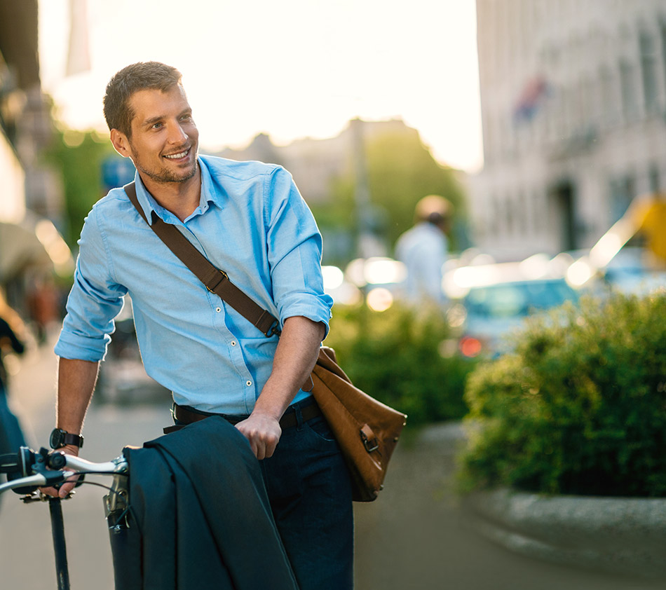 Young professional smiling, walking his bike with a jacket over the handle bars