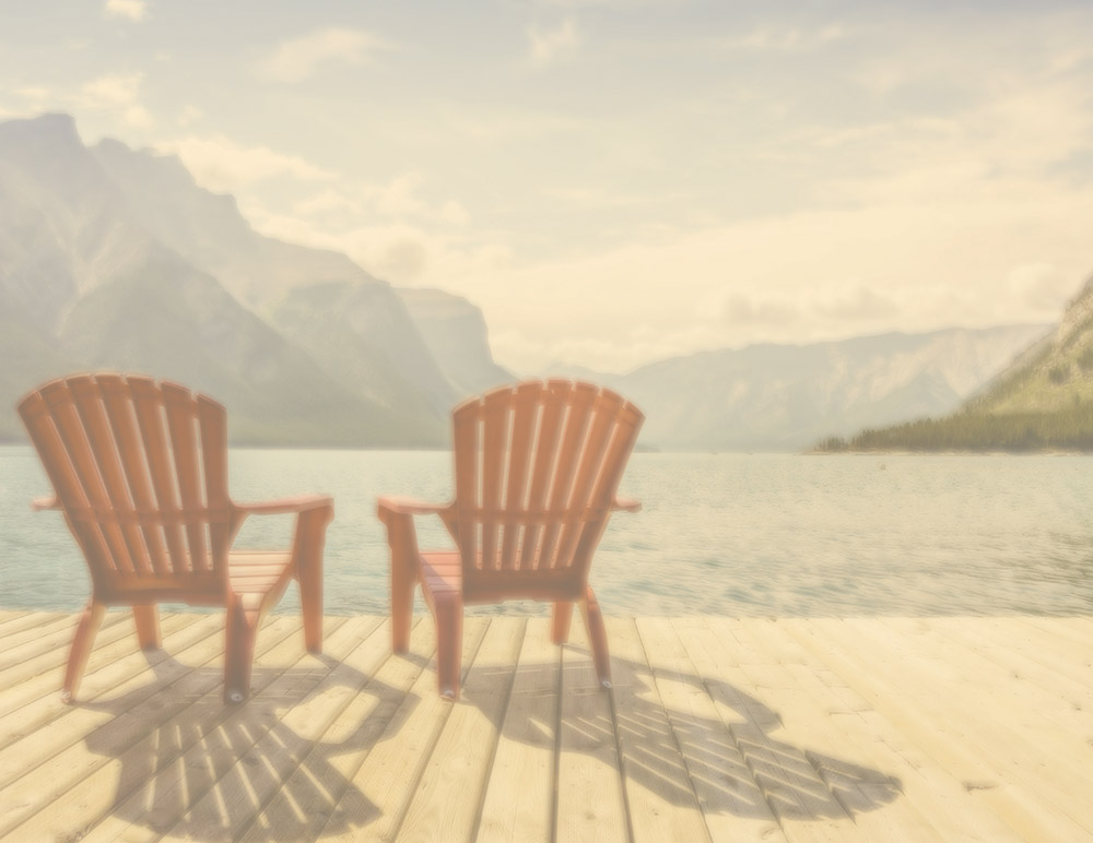 red adirondack chairs on a dock by the lake with mountains in the background