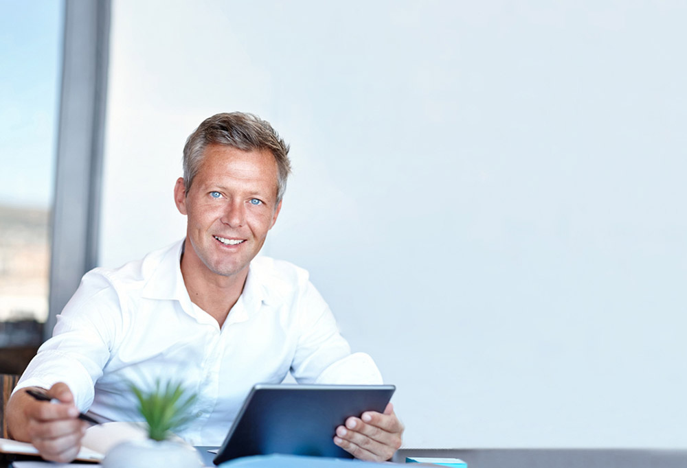 Mature man reading tablet, smiling at the camera